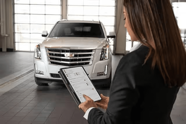 A businesswoman using a tablet to check vehicle features in a modern showroom with a white luxury SUV in the background.