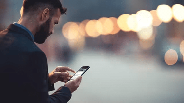 A man in a formal suit uses a smartphone while standing outdoors in a softly lit urban setting, showcasing a focus on technology and modern communication.