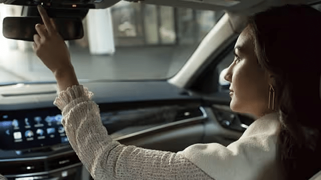A woman in a white sweater adjusting the overhead controls in a modern car, showcasing a sophisticated interior with a digital dashboard and infotainment system.