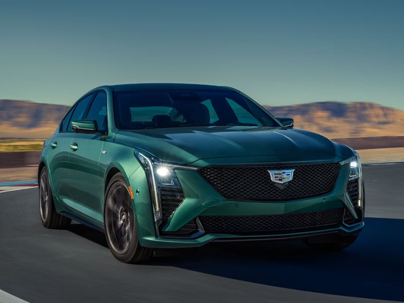 Sleek green Cadillac CT5-V Blackwing sports sedan on a racetrack, showcasing its aggressive design, high-performance features, and modern styling against a mountainous backdrop.