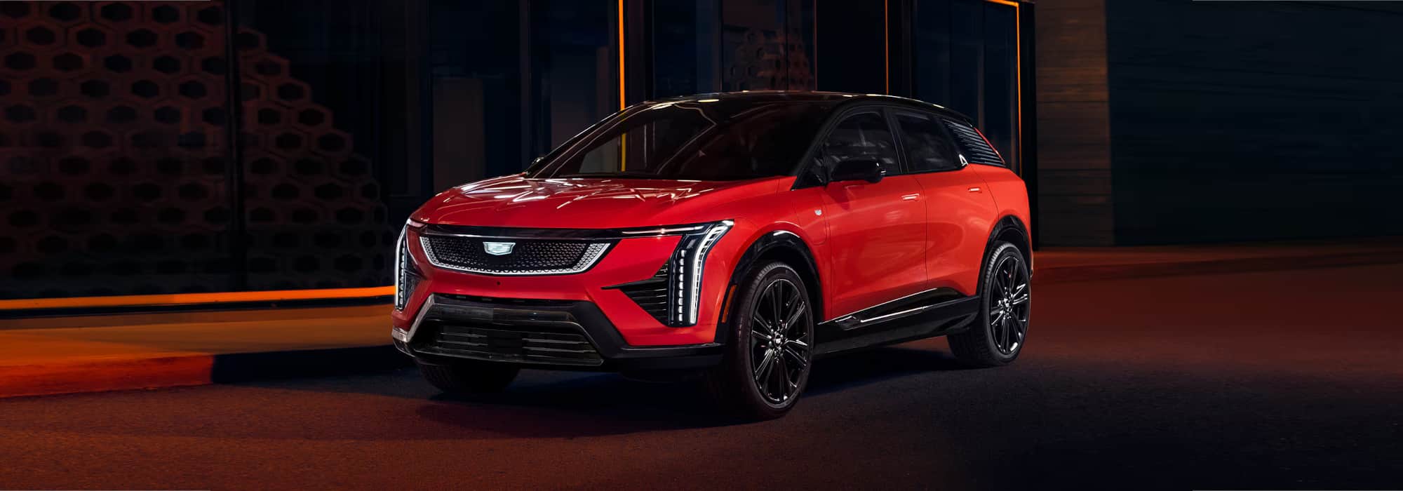 A sleek red Cadillac electric SUV parked at night, showcasing modern design features and dynamic lighting against a dark urban background.
