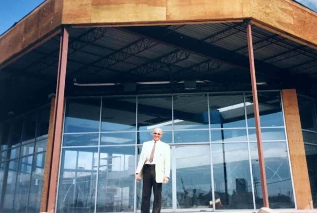 A man stands in front of a modern commercial building with large glass windows and a rust-colored facade, showcasing contemporary architectural design and construction features.