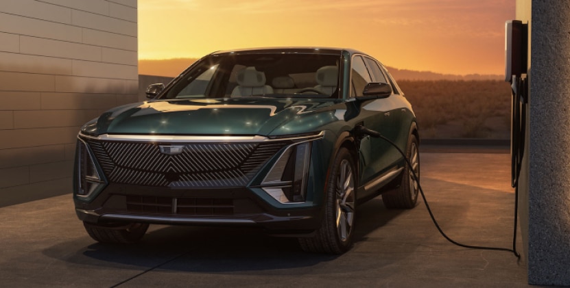 Electric Cadillac SUV charging in a modern setting at sunset, showcasing its sleek design and advanced features.