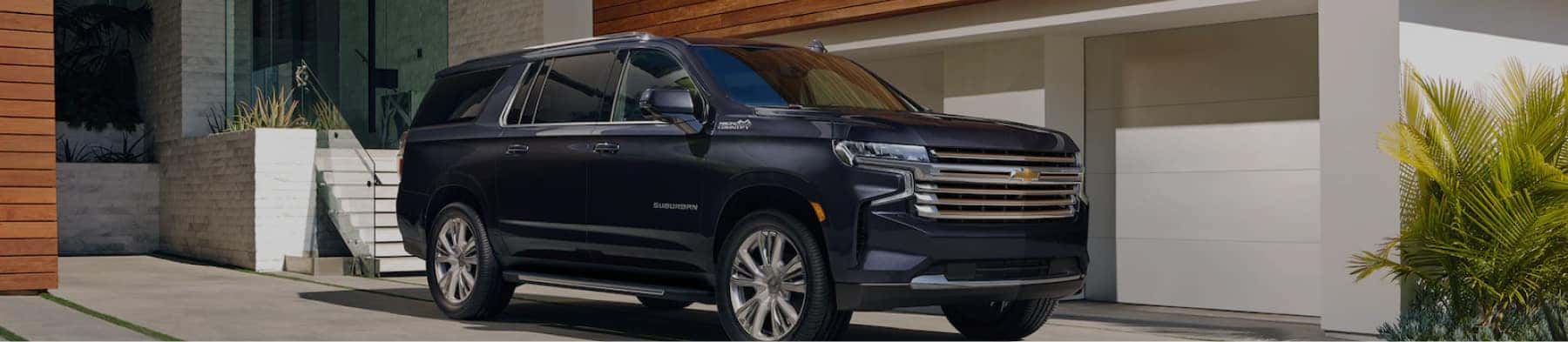 Chevrolet Suburban parked in a modern driveway, showcasing its sleek design and luxury features, surrounded by contemporary architecture and landscaping.