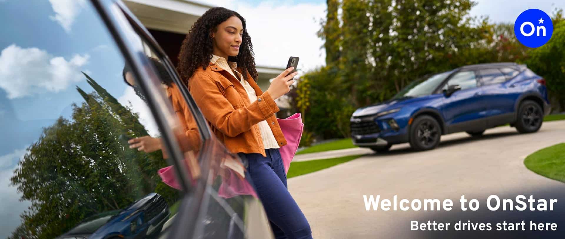 A young woman in a brown jacket is using a smartphone while standing next to a parked blue SUV in a suburban setting, showcasing the convenience and technology of OnStar services.