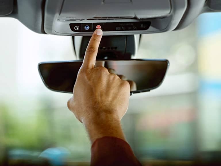 Hand pressing the emergency button on a car's overhead console, with a focus on safety features and vehicle technology.