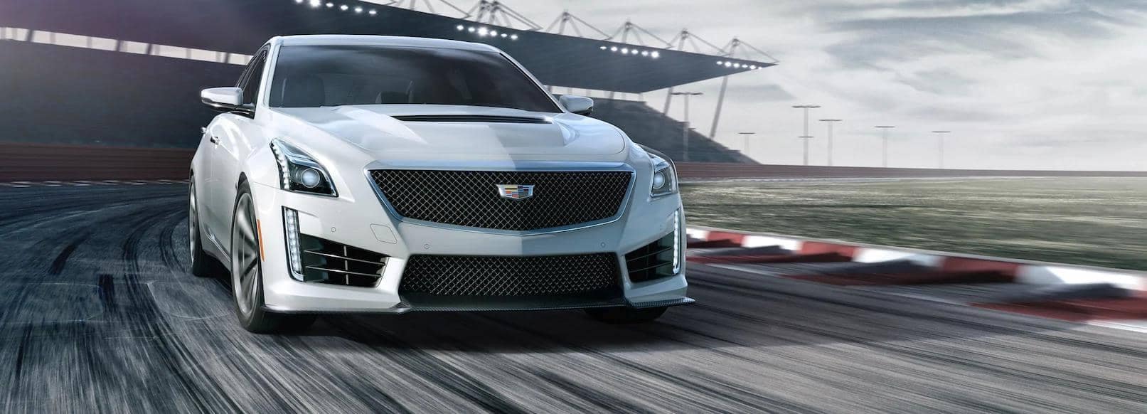 High-performance white Cadillac CTS-V racing on a track, showcasing its sleek design, powerful front grille, and dynamic speed in a competitive motorsport environment.
